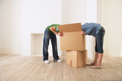 Νεαρό ζευγάρι αποσυσκευασία κουτί σε νέο σπίτι με κρυμμένα πρόσωπα