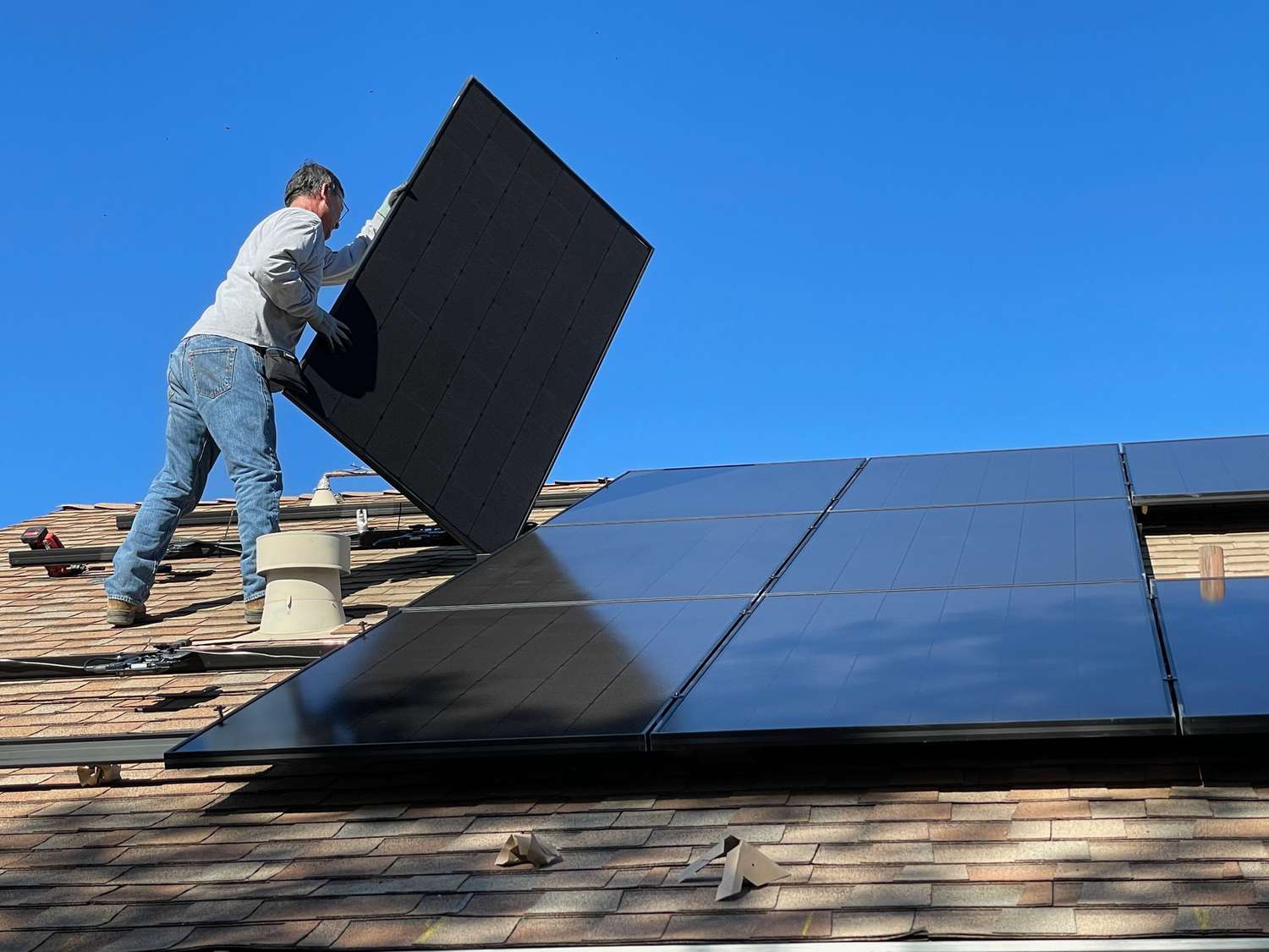 άνθρωπος που εγκαθιστά ηλιακούς συλλέκτες στη στέγη ενός σπιτιού
